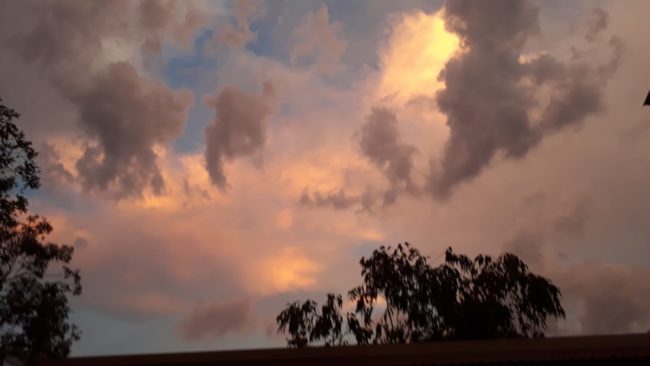Dunkle Wolken türmen sich im vom Sonnenuntergang in den gelb, orange und rot gefärbten Himmel