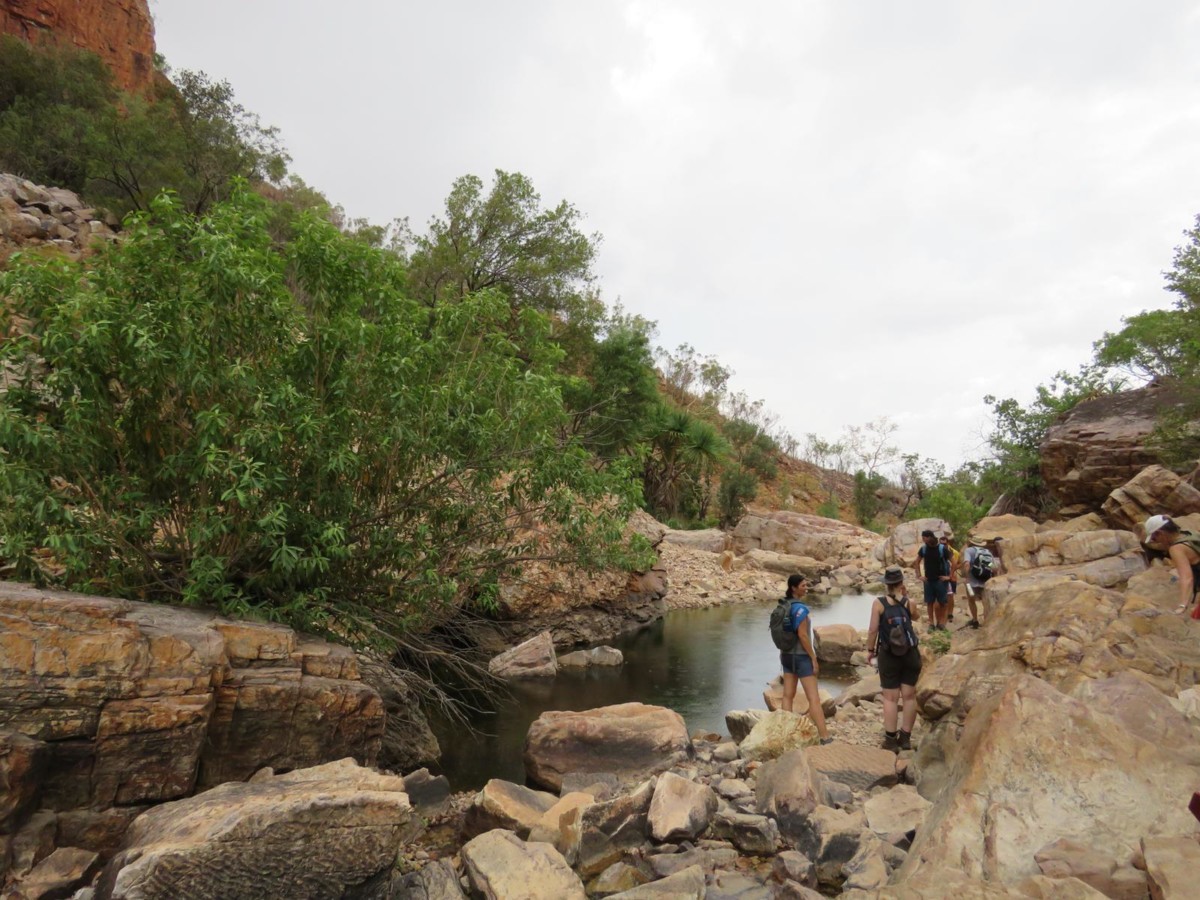Eine Reisegruppe spaziert entlang eines Flussbettes durch eine schroffe Felslandschaft