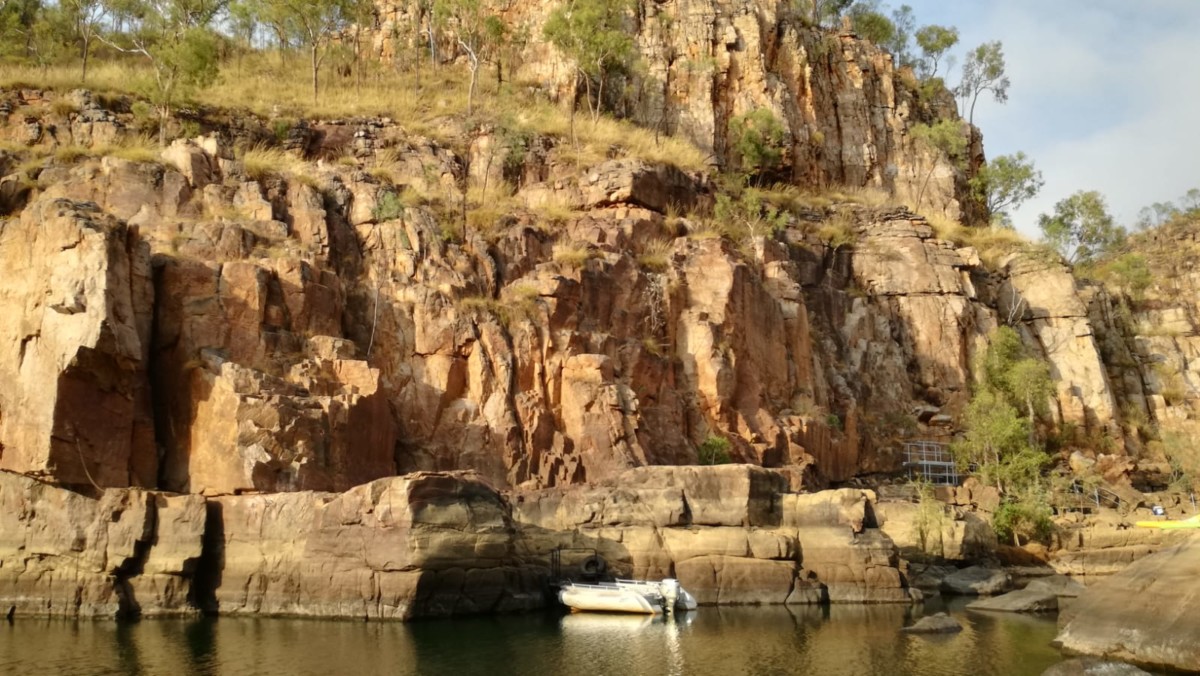 kleines Motorboot ankert vor steilaufragenden Felsen, die mit Grad und Gebuesch bewachsen sind