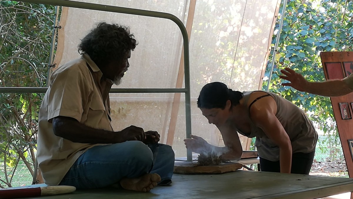 Aborigine sitzt auf einer Pritsche und fuehrt eine Rauchzeremonie durch