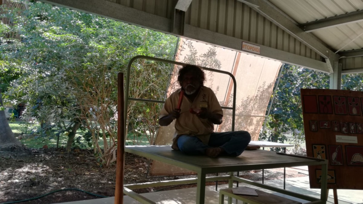 Aborigine sitzt auf Pritsche und schlaegt clapsticks zusammen